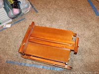 Folded wooden portable travel easel laid on carpet showing warm wood finish and folding parts