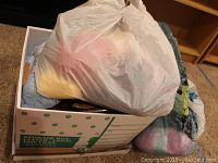 Box filled with multiple skeins and balls of colorful new yarn, some in plastic bags.