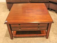 Front view of square wooden coffee table showing drawer and lower shelf, minor scratches visible on surface.