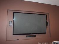 Full front view of TV mounted on wall with speakers visible on sides