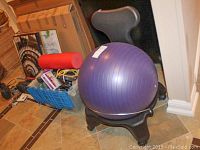 Purple yogaball placed on a black chair base with wheels, along with blue storage box containing miscellaneous items and a red foam roller in the background.
