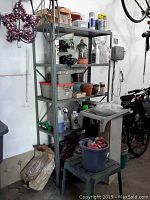 Front-left angle view of gray metal shelving unit with various items on shelves, showing sturdiness and minor wear on frame.