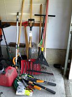 Overall view of yard tools showing rake, shovel, gas can, hand saw, and other items leaning against wall in garage.