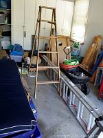 Wooden step ladder standing with aluminum extension ladder laid on the floor alongside various garage items.