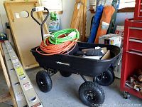 Black Gorilla Carts garden dump cart with black plastic bed holding coiled extension cords and various items. Four large air tires visible, cart frame in good condition with minor scratches.