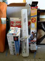Photo showing boxed Bissell Spot Cleaner, LiteEater Dryer Vent Cleaning System box, and tall white work light with protective cage and power cord