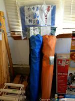 Photo of two rolled tarps, one blue and one orange, with boxed blue tarp and cover packaging on top