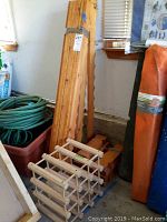 Two wooden wine racks leaning against a wall, one assembled and one unassembled flat pieces