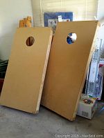 Front view of two wooden cornhole boards leaning against wall showing circular holes and board surface.