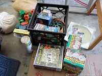 Wide shot showing black crate with coiled garden hose, boxed kids stepping stone kits, white plastic lanterns, and loose bug repellent sprays and insect repellent products nearby