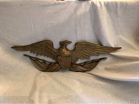 Full view of vintage American eagle wall plaque with gold finish, wings spread wide, shield in center, and draped flags below.