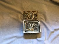 Image of two rectangular cherub trays, one nested inside the other, showing raised cherub designs and decorative borders.