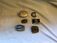 Top view of six assorted belt buckles showcasing different designs including floral engraved, horseshoe, trout fish, and decorative motifs.