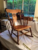 Side front angle of the antique wooden rocking chair showing decorative backrest and replaced seat.