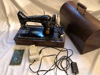 Singer 100th Anniversary sewing machine, foot pedal, electrical cords, and wooden carrying case on a beige background.