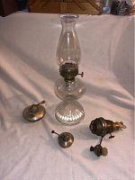 Full view of antique glass oil lamp with four additional wick mechanisms (one Aladdin and three silverplate) arranged around it on a fabric surface.