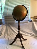 Front angled view of the antique globe on tripod stand, showing the globe's size relative to surroundings and detail of wooden stand and metal meridian ring.