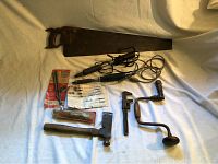 Full layout of the antique tool collection showing saw, soldering irons, socket wrench, hand crank drill, hatchet, and associated tools and documents