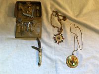 Photo showing all four items together on fabric: the closed leather pouch with tools, the pocket knife, and both medals with chains.