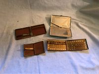 Photo of four vintage cigarette cases open, showing different interior linings and materials under soft lighting on fabric background.