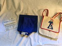 Two bags laid flat, blue Danna bag with folded bandanna on left, cream canvas "love is" bag on right.
