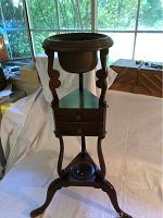 Front and side view of the antique cigar stand showing wooden structure, two drawers, copper ashtray bowl, and tripod base.