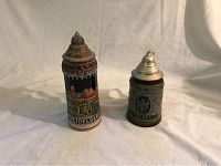 Photo showing two vintage German beer steins from Heidelberg and Österreich side by side on cloth backdrop.