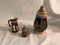 Photo showing all three vintage beer steins ranging from small to large including a brown stein with white relief and two painted steins with pewter lids.