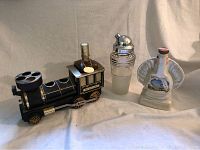 Full view showing the three items in the lot: black Iron Horse 1880 train canister, glass cocktail shaker with chrome top, and white seashell-shaped canister bottle with label.