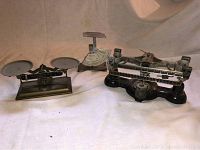Three antique and vintage scales displayed together showing different styles and sizes, placed on white cloth background.