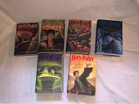 Set of six Harry Potter books laid out on a surface, showing front covers clearly. Includes Chamber of Secrets, Goblet of Fire, Prisoner of Azkaban, Order of the Phoenix, Half-Blood Prince, and Deathly Hallows.