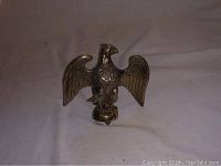 Metal eagle figurine with wings spread, detailed feathers, standing on a round base with a threaded screw