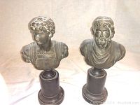 Pair of two dark-colored bust statues on black pedestal bases.