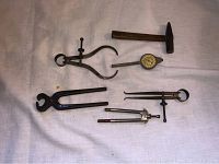 Antique drafting tools including hammer, dial gauge, clamp clippers, calipers, compass.