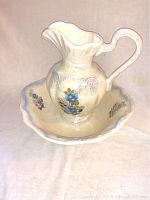 Photo of ceramic pitcher and basin with visible blue rose decorations and oyster white background.