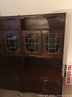 Front view of a single vintage wooden showcase cabinet showing glass doors with metal trim and a solid bottom door.