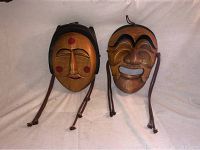 Photo of two vintage wooden oriental face wall hangers, showing front view with facial features, natural wood finish, and hanging cords.