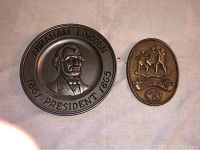 Photo showing both wall plaques side by side on a white fabric background.