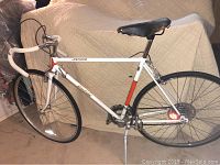 Side view of vintage Raleigh Record road bicycle, shows full frame with white and orange paint, leather saddle, drop handlebars, and wheels.