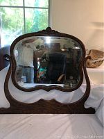Photo showing tiger wood dresser top mirror with carved top floral detail and curved edges, mirror leaning against wall.