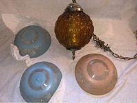 Photo of main amber glass hanging lamp alongside three separate glass chandelier covers in blue and peach shades.
