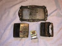 Full set of antique cigarette kit items displayed on cloth background, including metal tray, cigarette case, ashtray with removable cover, and batch book holder, all with floral patterns.