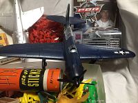 Photo showing dark blue model airplane, silver airplane, Pick-Up Sticks container, and boxed set of cowboy, Indian, fireman toy soldiers in multiple colors