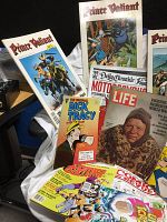 Photo showing Prince Valiant comic books, Dick Tracy magazines, Motorpsycho mini poster, and Life magazine arranged on a surface with a white cloth.