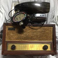 Front view of the antique Zenith radio with miscellaneous items on top including vacuum cleaner, clock, and electronic device.