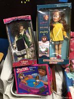 Photo showing the Collectors Choice bisque porcelain doll in Victorian-style dress, Barbie Bubbling Spa boxed playset, and the Babysitters Club doll in original packaging.