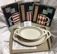 Set of three metal wall art plaques with coffee mugs, two nested white Corning Ware oval baking dishes, and one rectangular beige baking tray visible in front.