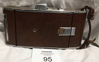 Side view of vintage Polaroid Land Camera with closed leather exterior and metal clasp, revealing brown leather strap and some wear on the leather surface.
