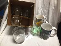 Photo showing four glasses packed in a cardboard box, one additional clear glass with Santa Anita logo, a large beer mug, and a ceramic horse racing mug.