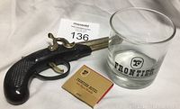 Three items shown together: a pistol-style lighter, a glass with Frontier logo, and a matchbook from Frontier Hotel